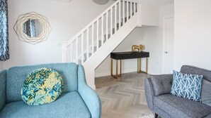 A modern living room with a staircase, a round mirror, and two sofas with patterned cushions.