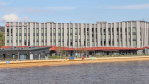 A modern hotel with a flat roof and a large water body in front.