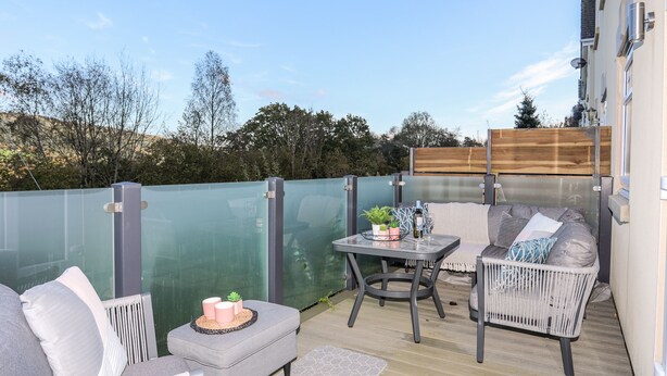 An outdoor patio with a glass enclosure, grey furniture, and a table with a plant and glassware.