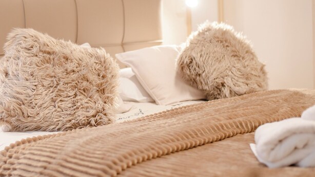 Una cama con almohadas beiges mullidas y un edredón beige con textura.