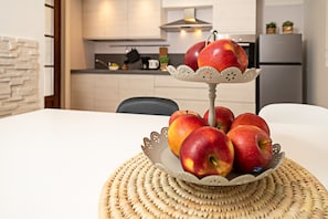 A dining table with a decorative fruit stand holding several apples, a woven placemat, and a kitchen in the background.