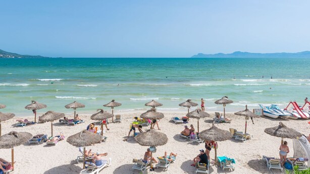 Una playa con sombrillas de paja, sillas de descanso y una vista despejada del mar.