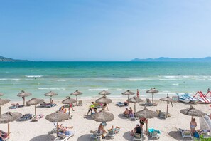 Ein Strand mit reetgedeckten Sonnenschirmen, Liegestühlen und freiem Blick auf das Meer.