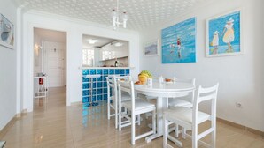 Una cocina moderna con armarios blancos, una isla central y una zona de comedor con sillas blancas y una mesa redonda.