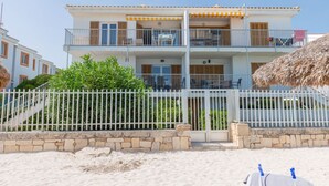 Un edificio de dos pisos con un balcón, una cerca blanca y una playa al frente.