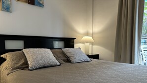 Un lit bien fait, avec une couvre-lit à motifs et deux oreillers, une lampe de chevet et une vue sur l’extérieur par la fenêtre.