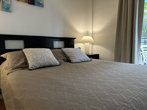 Un lit bien fait, avec une couvre-lit à motifs et deux oreillers, une lampe de chevet et une vue sur l’extérieur par la fenêtre.