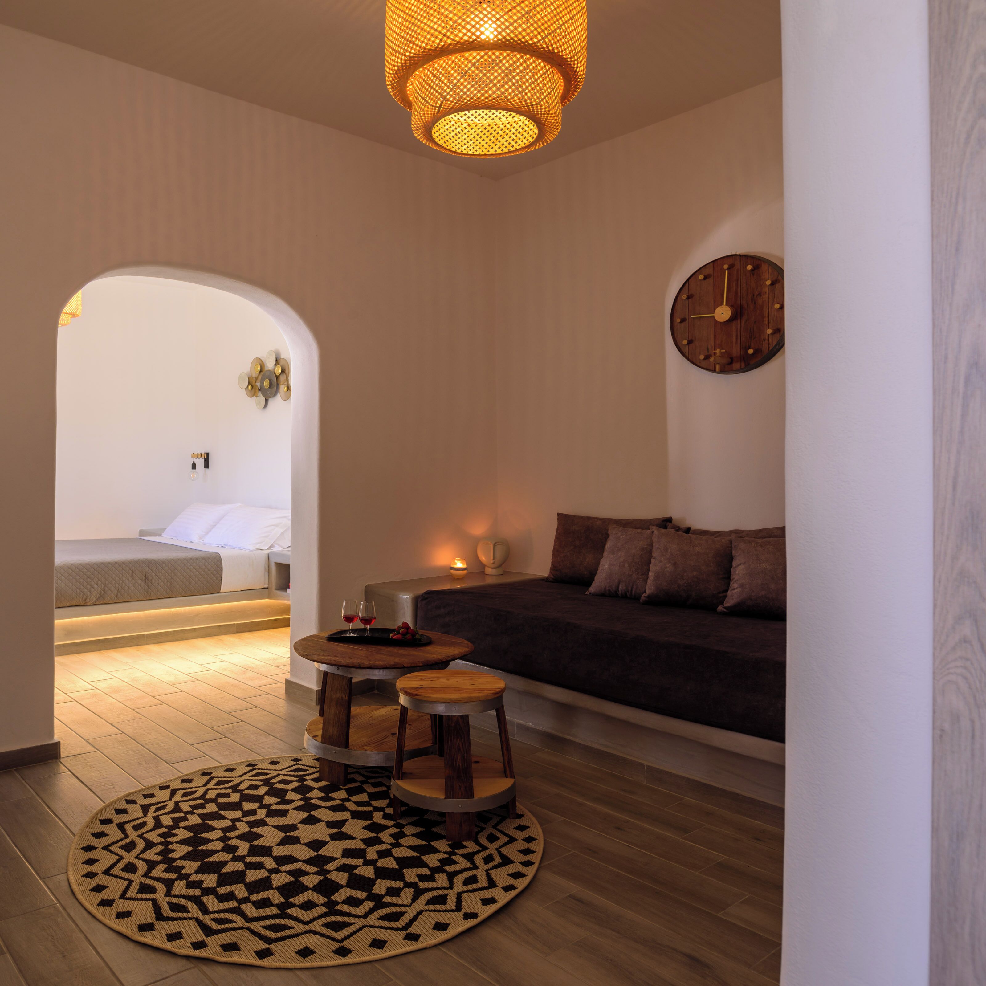 A modern, well-lit room with a round wooden table, a patterned rug, a sofa, and a wall clock.
