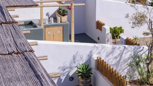 A rooftop terrace with a view of the sea, featuring white walls, wooden pergolas, and potted plants. - Athiri Luxury Suites Perivolos (Santorini)