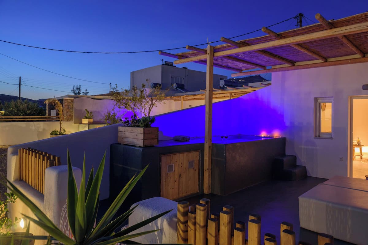 A modern outdoor patio with a wooden pergola, a hot tub, and a seating area with cushions.