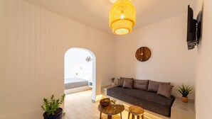 A modern living room with a sofa, two wooden side tables, a potted plant, and a hanging light fixture. - Athiri Luxury Suites Perivolos (Santorini)