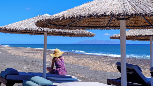 A beach with thatched umbrellas and lounge chairs. - Athiri Luxury Suites Perivolos (Santorini)