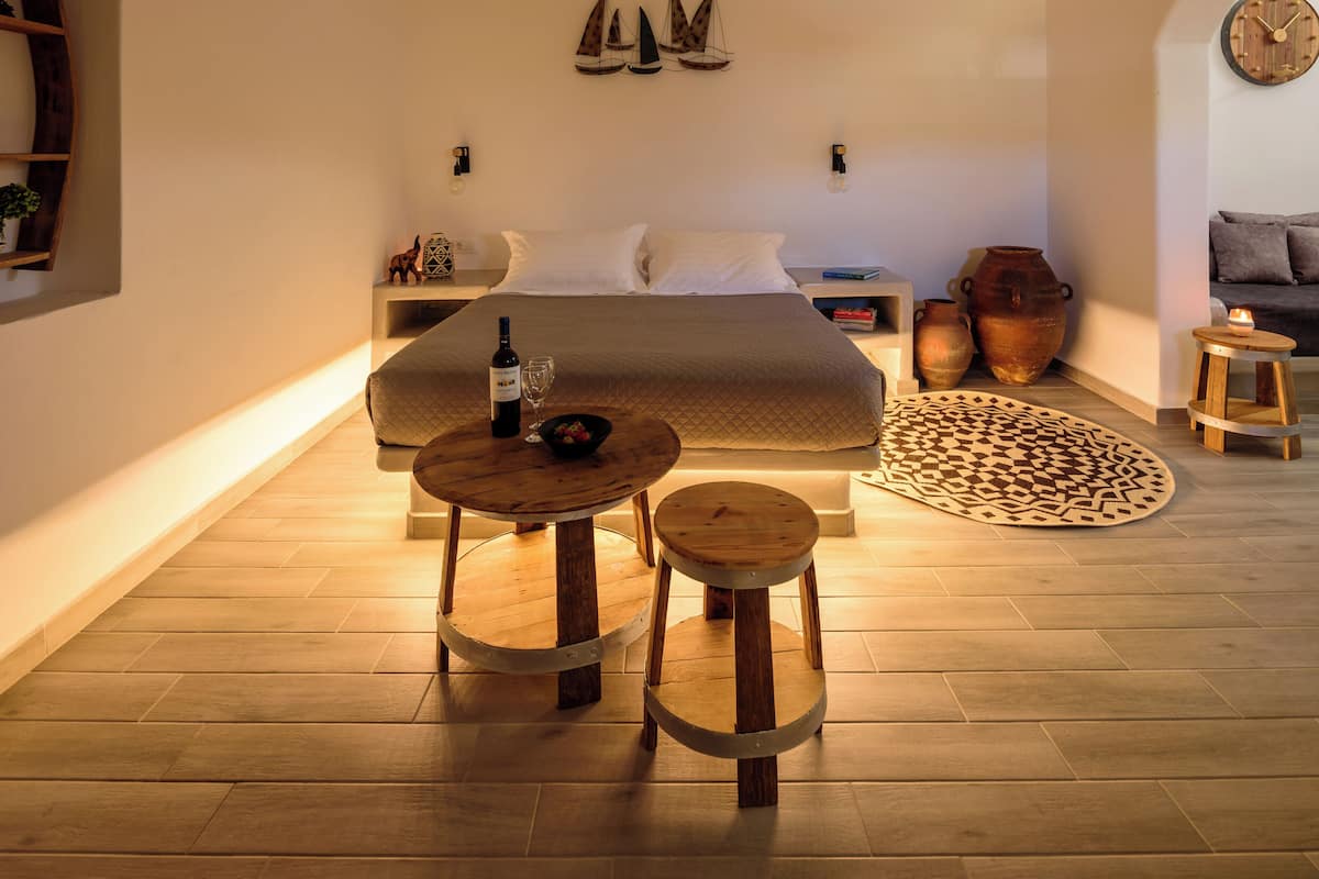 A spacious bedroom with a large bed, a bedside table with a bottle and glass, a small round table with a bowl, and a woven light fixture above.