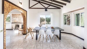 Une salle à manger spacieuse avec une grande table, des chaises blanches et une cheminée en pierre.