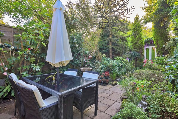 A glass-top table with wicker chairs and a white umbrella in a garden setting.