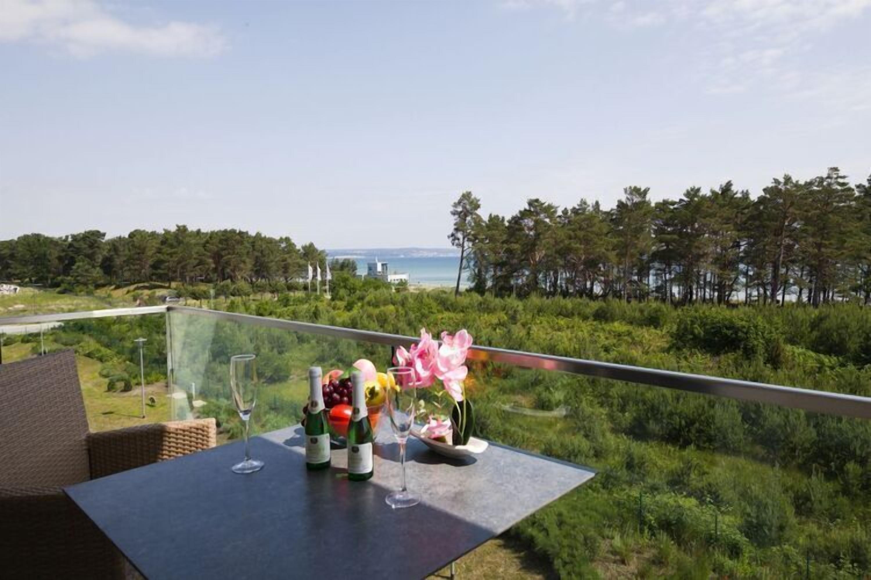 Un tavolo con bottiglie e un bicchiere su un balcone che si affaccia su un panorama pittoresco di alberi e mare.