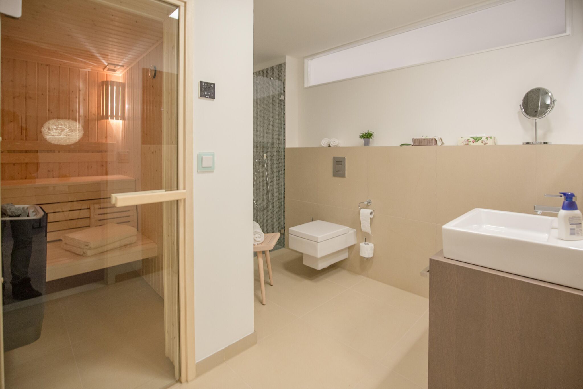 A modern bathroom with a glass-enclosed sauna, a toilet, a sink, and a mirror.