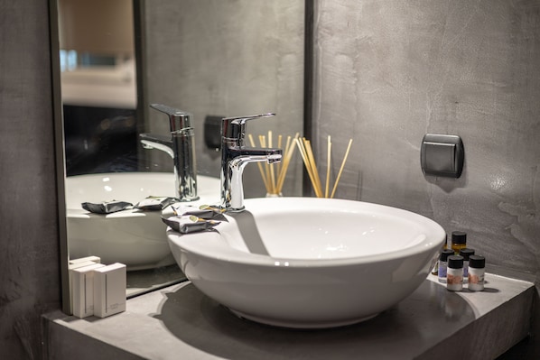 A modern bathroom with a large white sink, a chrome faucet, and a mirror. There are toiletries and a soap dispenser on the counter.