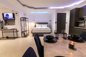 Habitació d'hotel moderna amb llit, televisió, taula de menjador amb espelma i zona de cuina.