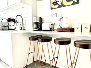 A modern kitchen with white cabinets, a coffee maker, a toaster, and a dish rack. There are four stools under the counter. - soho london suite (London)