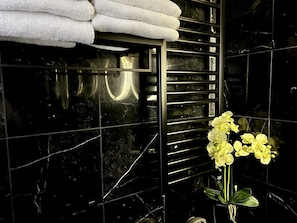 A bathroom with black marble tiles, a towel rack with folded towels, and a vase with yellow flowers. - soho london suite (London)