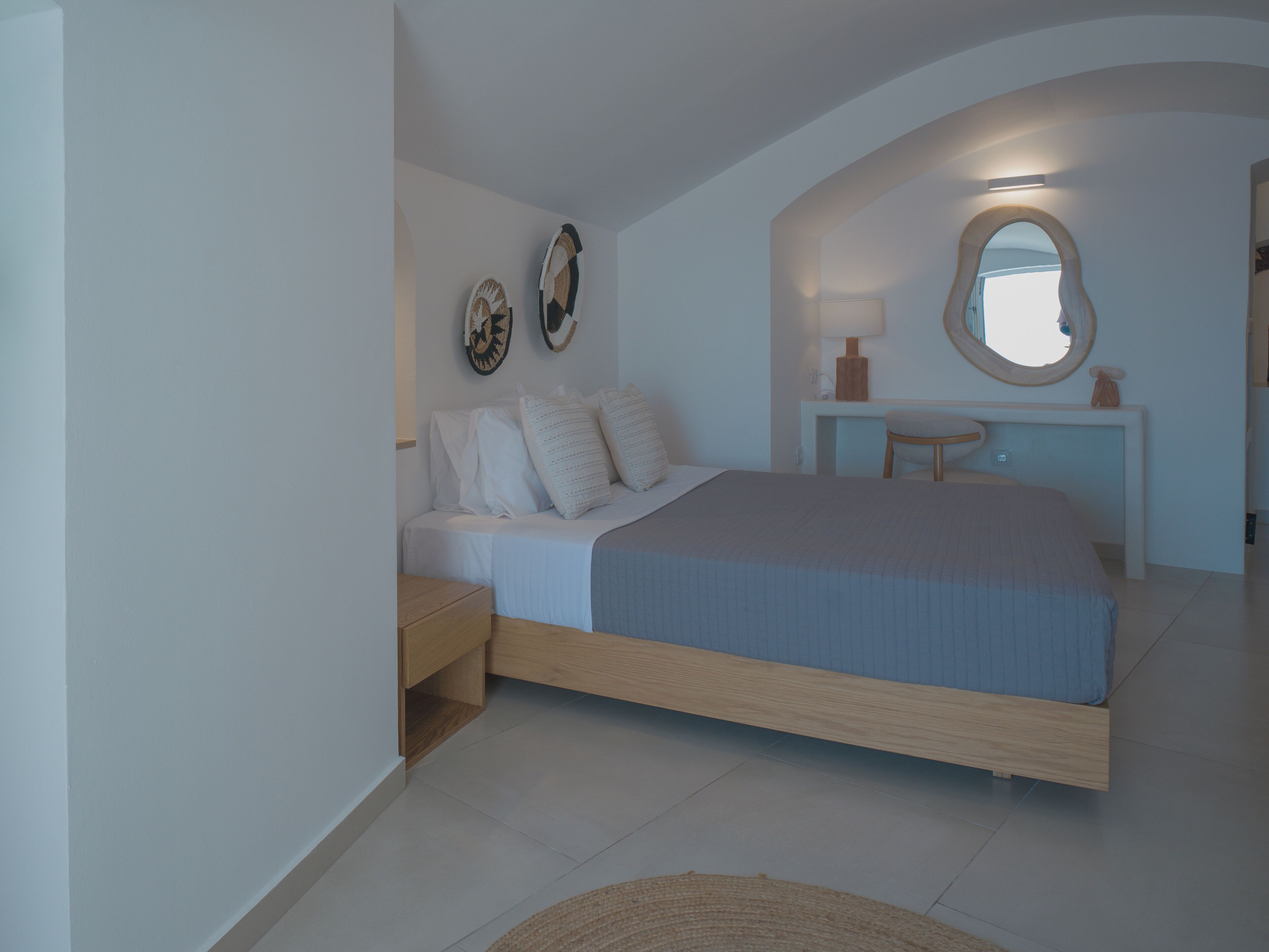 Un dormitorio con cama, mesitas de noche, tocador con espejo y decoración en la pared.