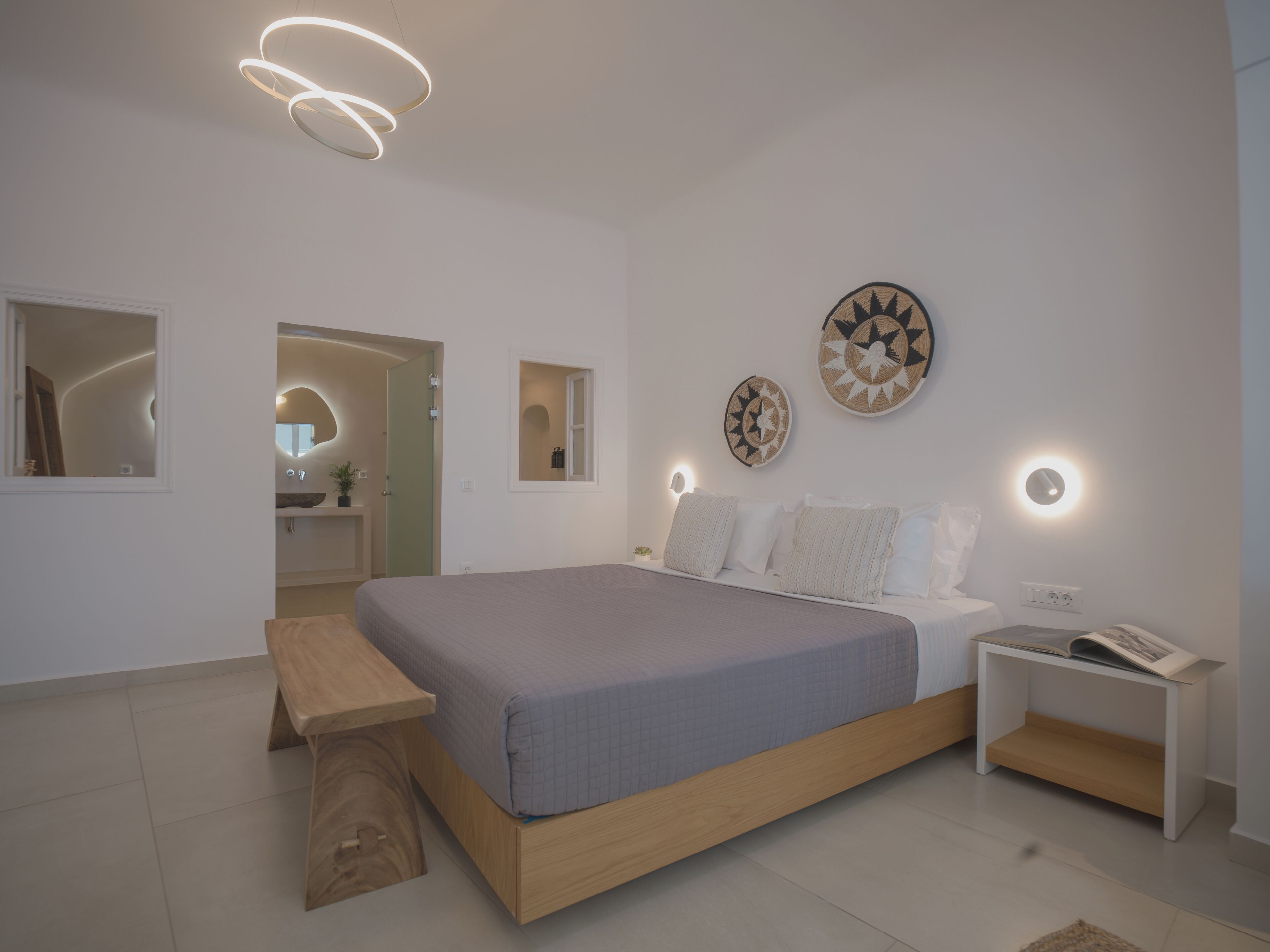 Un dormitorio moderno con una cama grande, mesitas de noche, un banco e iluminación en la pared.
