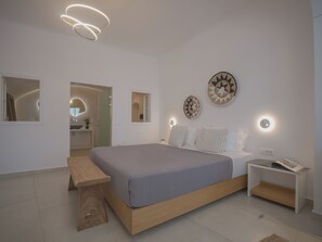 Un dormitorio moderno con una cama grande, mesitas de noche, un banco e iluminación en la pared.