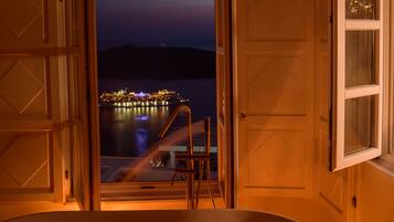 Puerta abierta que da a un balcón con vista a un barco iluminado por la noche.