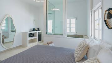 A modern bedroom with a large bed, a bedside table, a mirror, and a window.