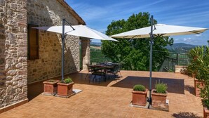 A stone building with a patio area featuring a table and chairs under large umbrellas, surrounded by potted plants. - Luxury villa in Vasciano (Todi - Umbria) with private pool and fantastic views (Vasciano)