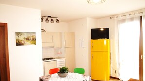 A compact kitchen with white cabinets, a yellow refrigerator, a dining table with chairs, and a painting on the wall. - Diana apartment, near the historic center bright and spacious (Oderzo)