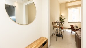 A modern living room with a round mirror, a wooden bench, a dining area with a table and chairs, and a large window providing natural light. - Lovely Cozy Nazionale 4 (Roma)