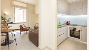 A modern kitchen with a built-in oven and a dining area with a brown leather couch and wicker chairs. - Lovely Cozy Nazionale 4 (Roma)