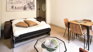 A bedroom with a bed, a dining table with chairs, a large framed picture on the wall, and a suitcase on the floor. - Lovely Cozy Nazionale 4 (Roma)