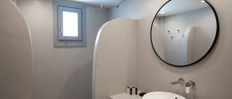 A modern bathroom with a large round mirror, a white sink, and a shower area.