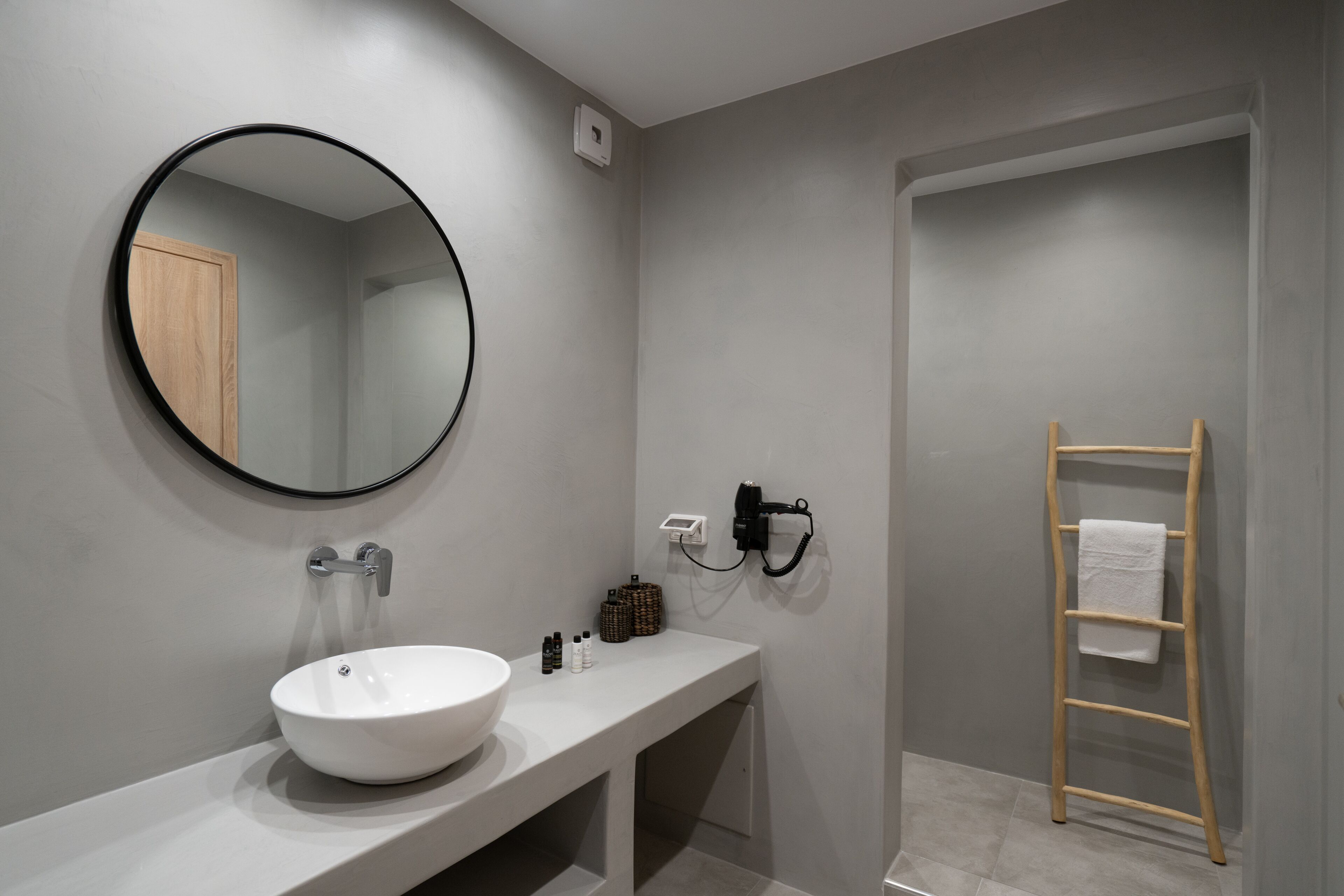A modern bathroom with a round mirror, a white sink, a towel rack, and a wooden ladder.