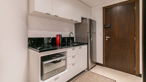 Eine kompakte Küche mit weißen Schränken, einem Edelstahl-Kühlschrank, einem eingebauten Backofen und einer schwarzen Arbeitsplatte.