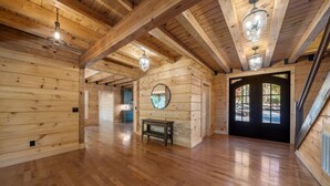 A spacious room with wooden walls and floors, a round mirror on the wall, and a bench. - Lake Lure's Newest Luxury Log Cabin Behind The Gates of Rumbling Bald Resort! (Lake Lure)