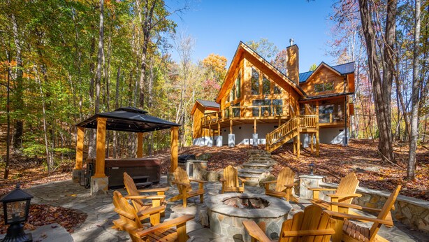A lodge with a stone fire pit and Adirondack chairs, surrounded by a forest. - Lake Lure's Newest Luxury Log Cabin Behind The Gates of Rumbling Bald Resort! (Lake Lure)