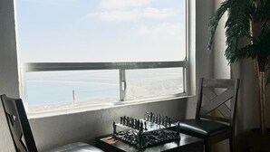 Un échiquier posé sur une table près d’une fenêtre donnant sur une plage.