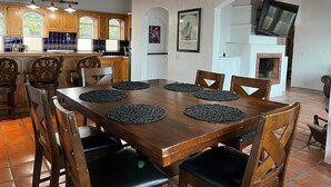Un coin repas avec une table et des chaises en bois, une cuisine à l’arrière-plan et une cheminée.