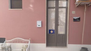 Un banco de metal blanco con cojines, una puerta gris con un adhesivo azul, una ventana pequeña y un cuadro de empalmes eléctricos fijado a la pared.