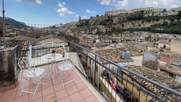 Una terraza con mesa y sillas, con vistas a un pueblo histórico con edificios en una colina y cielo despejado.