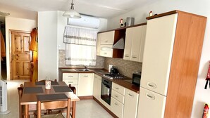 A compact kitchen with a dining table, wooden cabinets, a stove, and a microwave. - Spacious 3 bedroom apartment within walking distance from Bugibba seafront  (St. Paul's Bay)