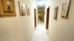 A hallway with artwork on the walls, leading to a room with a bed and a window. - Spacious 3 bedroom apartment within walking distance from Bugibba seafront  (St. Paul's Bay)