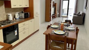 A compact kitchen with a stove, microwave, and cabinets. A dining table with chairs is set up in the center. - Spacious 3 bedroom apartment within walking distance from Bugibba seafront  (St. Paul's Bay)