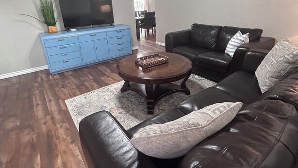 A living room with a dark leather sofa, a coffee table, a TV on a blue cabinet, and a ceiling fan. - The House with the Blue Door (Norman)