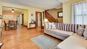 Ein Wohnzimmer mit einer Couch, einem Esstisch und Stühlen. Eine Treppe führt zu einer weiteren Ebene.