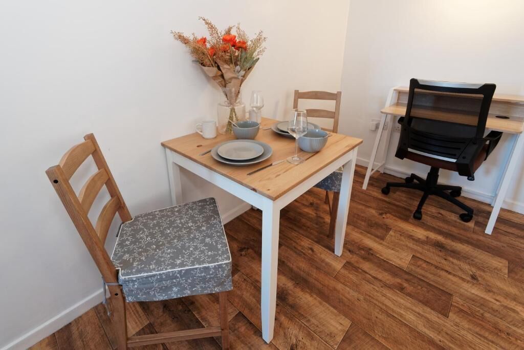 Een eetgedeelte met een houten tafel, twee stoelen, een vaas met bloemen en een zwarte bureaustoel.